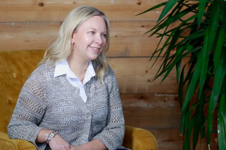 Inheritance disputes A woman with blonde hair smiles while seated next to a green plant in a wooden setting.